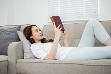 Bir kadın kanepede kitap okuyor. Gülümsüyor ve kitabının tadını çıkarıyor.