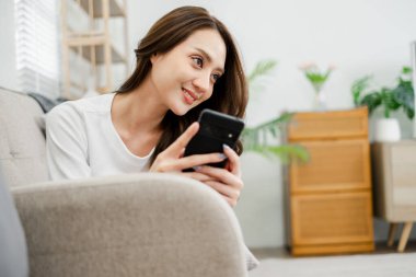 Bir kadın kanepede oturuyor ve cep telefonuna bakıyor. Gülümsüyor ve eğleniyor.