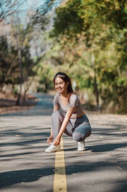 Bir kadın yolda diz çöküyor, ayakkabılarını giyiyor. Gülümsüyor ve eğleniyor.
