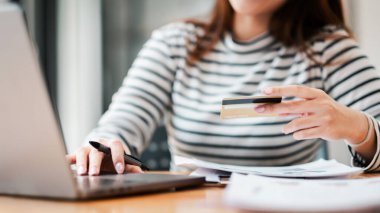 A woman is using a laptop to pay for something with a credit card. She is holding the card in her hand and she is focused on the task at hand