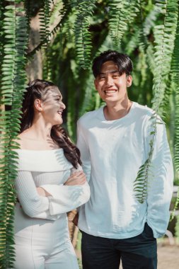 Bir adam ve bir kadın yemyeşil bir ormanda kameraya gülümsüyor. Adam beyaz bir gömlek giyiyor ve kadın beyaz bir elbise giyiyor. Sahne mutlu ve neşeli.