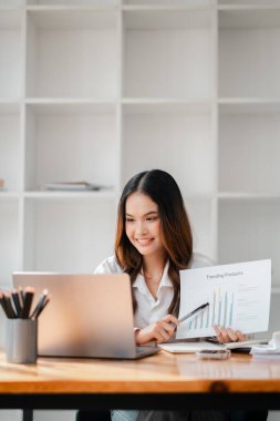 Bir kadın elinde laptop ve sunum kağıdıyla masada oturuyor. Gülümsüyor ve sunum kağıdını işaret ediyor.