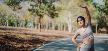 Bir kadın yolda geriniyor. Gri bir gömlek ve siyah pantolon giyiyor. Yol boş ve etrafta başka kimse yok.