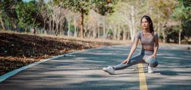 Bir kadın yol kenarında geriniyor. Gri bir gömlek ve gri pantolon giyiyor.