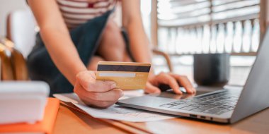 Bir kadın kredi kartıyla ödeme yapmak için dizüstü bilgisayar kullanıyor. O bir sandalyede oturuyor ve yanında bir fincan var.