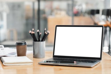 Bir dizüstü bilgisayar bir kalem tutacağı ve bir fincan kahveyle bir masanın üzerinde oturur. Laptop açık ve ekran boş. Sahne sessiz ve odaklanmış bir çalışma ortamı öneriyor.
