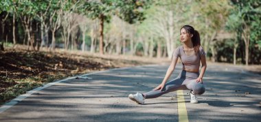 Bir kadın yol kenarında geriniyor. Gri bir gömlek ve gri pantolon giyiyor.