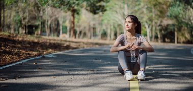 Bir kadın elinde bir şişe suyla yol kenarında oturuyor. Koşuya biraz ara verdi.