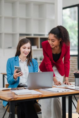 Modern bir ofiste laptoplar ve akıllı telefonlarla işbirliği yapan, takım çalışması ve üretkenlik sergileyen iki iş kadını..