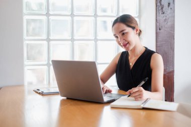 Profesyonel bir kadın dizüstü bilgisayarda çalışıyor ve modern bir ofiste not alıyor..