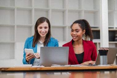 Modern bir ofiste birlikte çalışan, laptoplar ve tabletler kullanan, gülümseyen ve verimli bir işbirliği içinde olan iki profesyonel kadın..