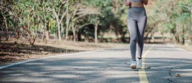 Sabahları parkta koşan, atletik kıyafetler giyen, spor yapmayı teşvik eden ve sağlıklı bir yaşam tarzı olan bir kadın..