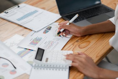 Bir kadın kalemle bir kağıt parçasına yazıyor. O bir hesap makinesi ve bir dizüstü bilgisayarla bir masada oturuyor. Masa kağıtlar ve diğer eşyalarla dolu.