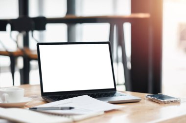 Masada bir fincan kahve ve cep telefonuyla birlikte bir dizüstü bilgisayar açık. Dizüstü bilgisayar ekranı boş ve masa kağıtlar ve diğer eşyalarla dolu. Olay yeri yoğun bir iş günü olduğunu gösteriyor.