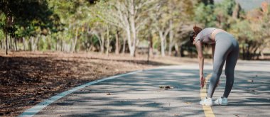Aktif giyinen bir kadın, bir sonbahar sabahı parkta esneyerek spor yapmayı ve sağlıklı bir yaşam tarzını teşvik ediyor..