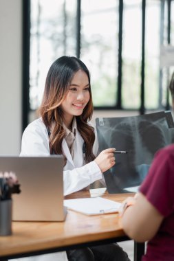 Gülümseyen bir kadın doktor, röntgen sonuçlarını modern ve parlak bir muayenehane ortamında hastaya açıklar..