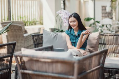 Genç bir kadın açık bir terasta hasır bir sandalyede rahat bir şekilde oturuyor, yemyeşil yemyeşil ile çevrili huzurlu bir anın tadını çıkarıyor..