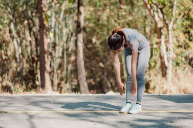 Ormanda güneşli bir günde spor kıyafetleri ve spor ayakkabıları giymiş koşuya ya da egzersiz rutinine hazırlanan bir kadın..