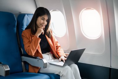Uçuş sırasında dizüstü bilgisayarda çalışan profesyonel bir kadın uçuş verimliliği ve rahat bir uçak kabininde modern seyahatler sergiliyor..