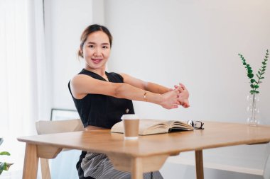 Modern bir ev ofisinde elinde kahve ve kitapla uzanan bir kadın. Doğal ışık ve yeşillikle aydınlık ve minimalist çalışma alanı.