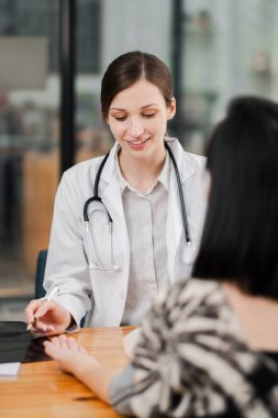 Modern bir muayenehanede bir hastaya danışmanlık yapan dost canlısı bir bayan doktor profesyonel sağlık hizmetlerine gülümseme sunuyor..