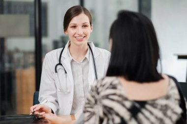 Modern bir muayenehanede bir hastaya danışmanlık yapan, profesyonel sağlık hizmetleri ve tıbbi tavsiyelerde bulunan dost canlısı bir bayan doktor..