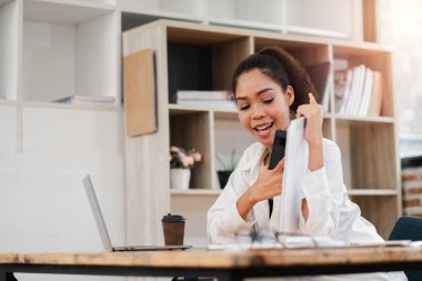 Evde çalışan genç bir kadın, telefonda gülümsüyor, konuşuyor, tablet tutuyor, bilgisayarlı modern çalışma alanı ve kahve fincanı var..