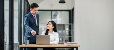 Modern ofis ortamında iki iş adamı bir masada dizüstü bilgisayarla tartışıyorlar..
