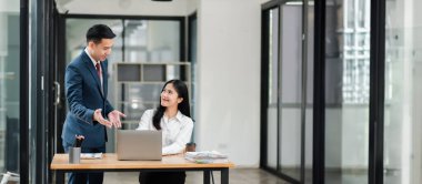 Modern ofis ortamında iki iş adamı bir masada dizüstü bilgisayarla tartışıyorlar..