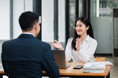 İki meslektaş modern bir ofiste verimli bir iş toplantısı yapıyor, bir dizüstü bilgisayar ve masadaki belgeleri tartışıyorlar..