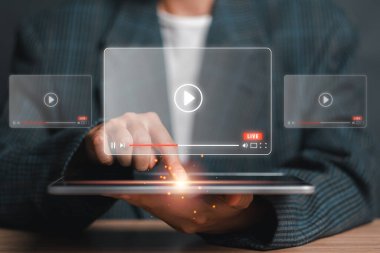 Bir kişi, modern teknoloji ve çevrimiçi medya tüketimini sembolize eden, gelecekçi bir video yayınlama arayüzünü gösteren dijital bir tabletle etkileşime giriyor.