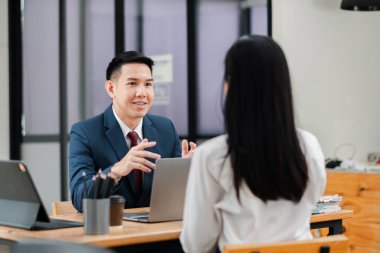 İki profesyonel iş görüşmesinde, modern bir ofiste laptopları ve belgeleri masaya koymayı tartışıyorlar..