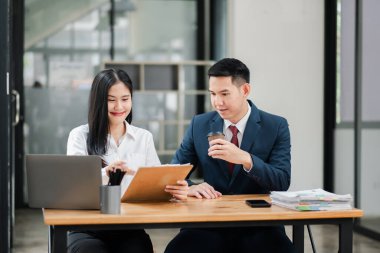 Modern ofis ortamında dokümanları tartışan iki profesyonel takım çalışması ve iş kıyafetleri sergileniyor..