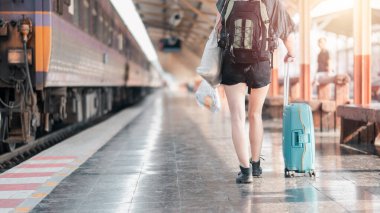 Sırt çantası ve bavuluyla genç bir gezgin tren peronunda yürüyor, gün doğumunda bir maceraya hazır..