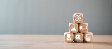 Tahta bir masaya istiflenmiş, bilim, teknoloji, mühendislik ve matematik kavramlarını temsil eden BTMM simgeleriyle tahta bloklar..