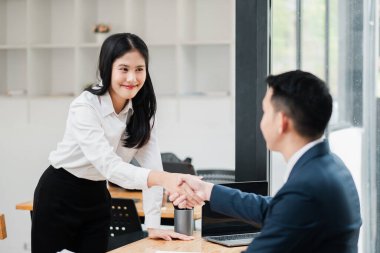 Modern bir ofiste el sıkışan iki iş adamı, anlaşmayı, ortaklığı ve başarılı işbirliğini simgeliyor..