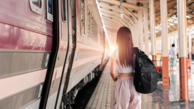 Gün batımında tren peronunda yürüyen sırt çantalı genç bir kadın seyahat ve maceranın özünü yakalıyor..