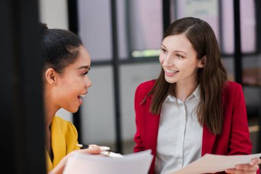 İki profesyonel kadın modern ofis ortamında üretken bir tartışma içinde, takım çalışması ve işbirliği sergiliyorlar..