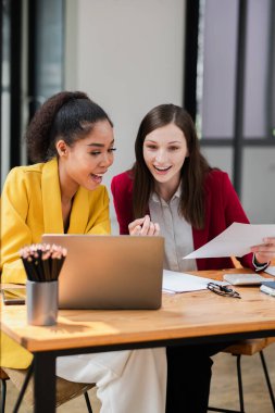 Çağdaş bir ofiste dizüstü bilgisayar kullanarak ve belgeleri inceleyerek birlikte çalışan iki profesyonel kadın..