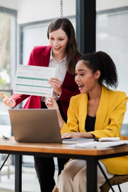 Günümüz ofis ortamında iş stratejilerini tartışan iki profesyonel kadın, dizüstü bilgisayar ve belge kullanıyorlar..