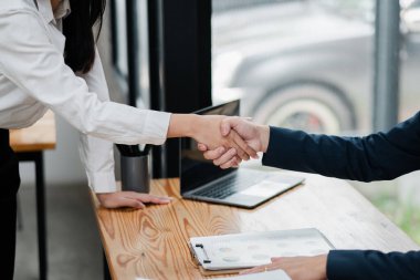 Modern ofis ortamında anlaşma ve ortaklığı sembolize eden iki iş adamı el sıkışıyor..