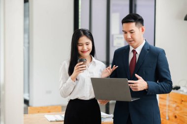 Modern ofis ortamında dizüstü bilgisayar kullanırken resmi giyinmiş iki iş adamı iş hakkında konuşuyor..