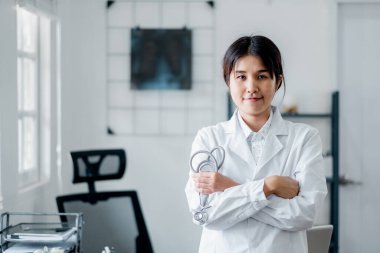 Beyaz önlüklü, steteskop tutan, modern bir muayenehanede duran kendine güvenen bir kadın doktor..