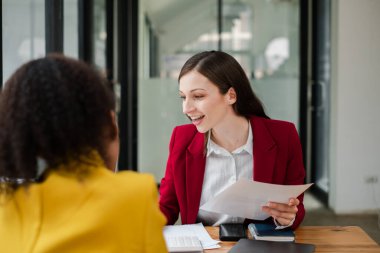 Modern ofis ortamında dokümanları tartışan iki profesyonel kadın iş görüşmesindeler..