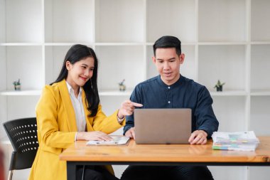 Çağdaş ofis ortamında dizüstü bilgisayarda birlikte çalışan iki iş adamı, belgeleri tartışıyorlar..