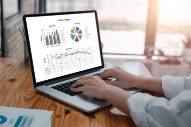 Finansal grafik ve grafikleri gösteren, çağdaş ofis ortamında veri analizlerini gösteren bir dizüstü bilgisayarda yazı yazan eller..