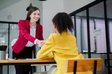 Modern bir ofiste el sıkışan iki profesyonel kadın başarılı iş ortaklığı ve işbirliğini simgeliyor..