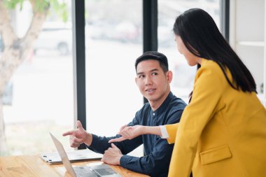 İki meslektaş, modern bir ofiste, geniş pencereli ve doğal ışık alan bir iş görüşmesi sırasında bir tartışmaya girdiler..