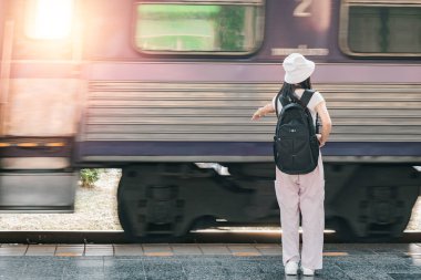 Sırt çantası ve şapka takan genç bir gezgin yaz mevsiminde tren istasyonunda bekliyor..