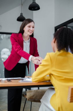 Modern ofis ortamında iş görüşmesinde profesyonel kıyafetli iki kadın el sıkışıyor..